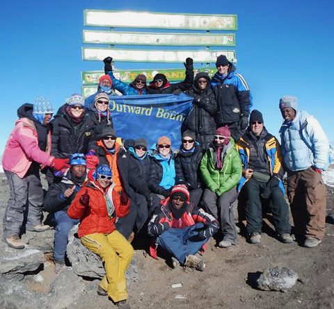 Group of climbers at the top of Mount Kilimanjaro holding an Outward Bound Canada flag 480x445