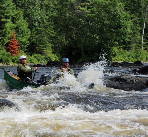 Participants in canoe paddling through white water 480x445