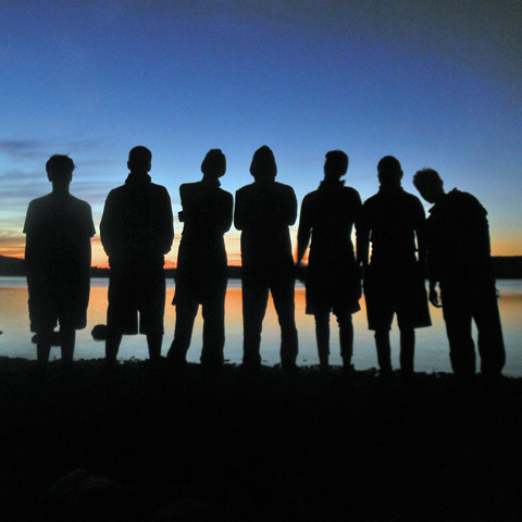 Silhouette-of-students-standing-on-shore-with-sunset-in-background