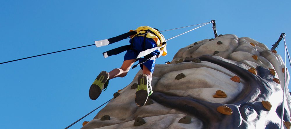 male student coming down from climbing the rock climbing wall 1 1000x445