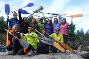Group of people holding canoe and kayak paddles over head