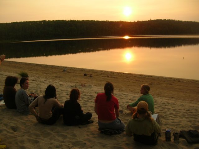 teens sitting on a beach at sunset