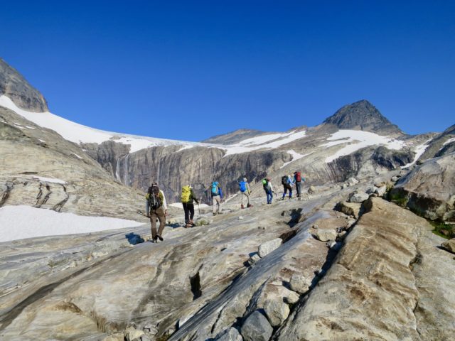 Seven people walking in a line through mountain peaks