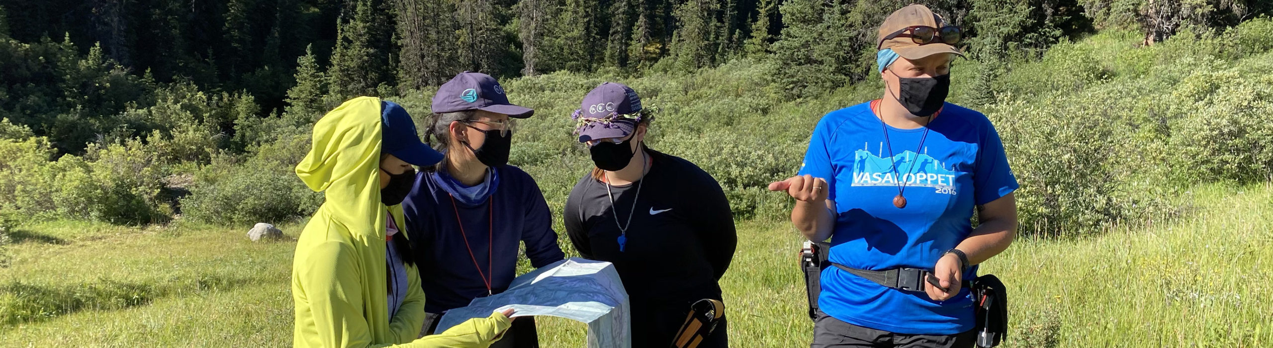 Four people wearing black masks and baseball caps looking at a map.