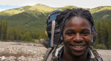 A backpacker smiling with mountains behind them.