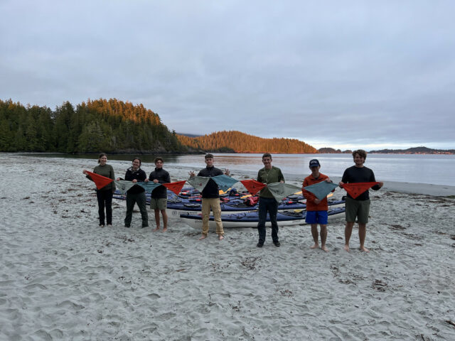 teens standing infront of kayaks on a beach